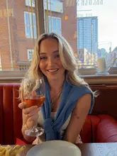 A portrait of a woman holding a glass of wine in a pub setting, with a plate of fries visible in the foreground. The image captures a relaxed, social atmosphere typical of a pub staycation.