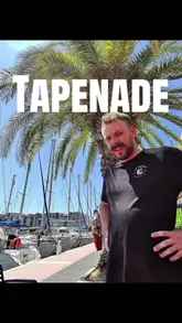 A travel-focused vlog where the creator visits a bar and cafe in Gruissan, France. The video features the creator interacting with staff, ordering local tapenade, coffee, and beer, and enjoying the scenic outdoor seating area overlooking the marina.