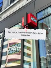 A photo of the exterior of the LEGO store in London, featuring a text overlay about affordable days out. The image captures the store signage but is heavily impacted by reflections of the surrounding buildings on the glass facade.