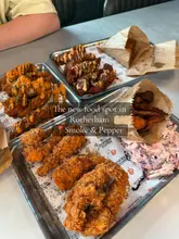 A top-down, slightly angled shot of multiple trays of fried chicken, wings, and sides from Smoke & Pepper in Rotherham, presented on branded paper.