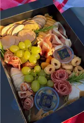 A group of friends enjoys a charcuterie board picnic on a beach, highlighting the product from The Flavour Merchant. The video features close-ups of the food, the friends interacting, and the scenic beach location.