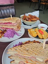 A vlog-style review of a garden centre cafe, showcasing their generously filled sandwiches, sides like salt and chili hash browns, and potato wedges, while also mentioning a summer sale.