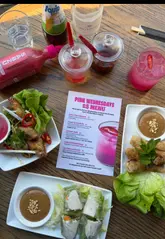 A creator reviews the 'Pink Wednesday' promotion at Pho, showcasing the £5 menu items including a spicy pink margarita, summer rolls, crispy chicken wings, and a new pink sriracha sauce. The video highlights the restaurant's gluten-free offerings and the fun, themed atmosphere of the promotion.