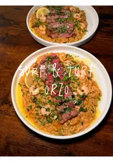 A fast-paced recipe tutorial demonstrating how to cook a surf and turf orzo dish, featuring steak and prawns, finished with chimichurri.