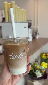 A short, energetic vlog-style video introducing a new coffee shop called Blondes in Kilrea. The creator walks the viewer through the exterior, the interior seating area, and highlights the selection of baked goods and coffee available.