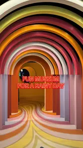 A symmetrical, eye-level shot of a colorful, arched tunnel at the TWIST Museum in London, featuring a text overlay promoting it as a fun rainy day activity.