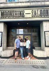 A group of friends visits the Moonshine Saloon in London, an immersive bar experience where guests 'smuggle' in their own alcohol, dress up in western-themed costumes, and play card and dice games while enjoying cocktails.