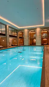 A high-quality, wide-angle shot of an indoor swimming pool at a luxury hotel, showcasing the elegant, architectural design and serene atmosphere of the spa.