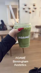 A casual, user-generated style shot of a matcha latte in a branded takeaway cup held by a customer at FOAMÉ in Birmingham. The image is functional but lacks professional polish, with flat lighting and a cluttered background.