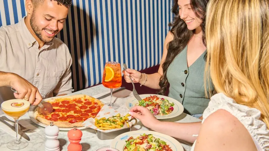 Friends sharing pizza, salads and cocktails over lunch at a restaurant table