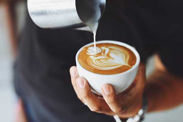 A barista pours some latte art on a flat white